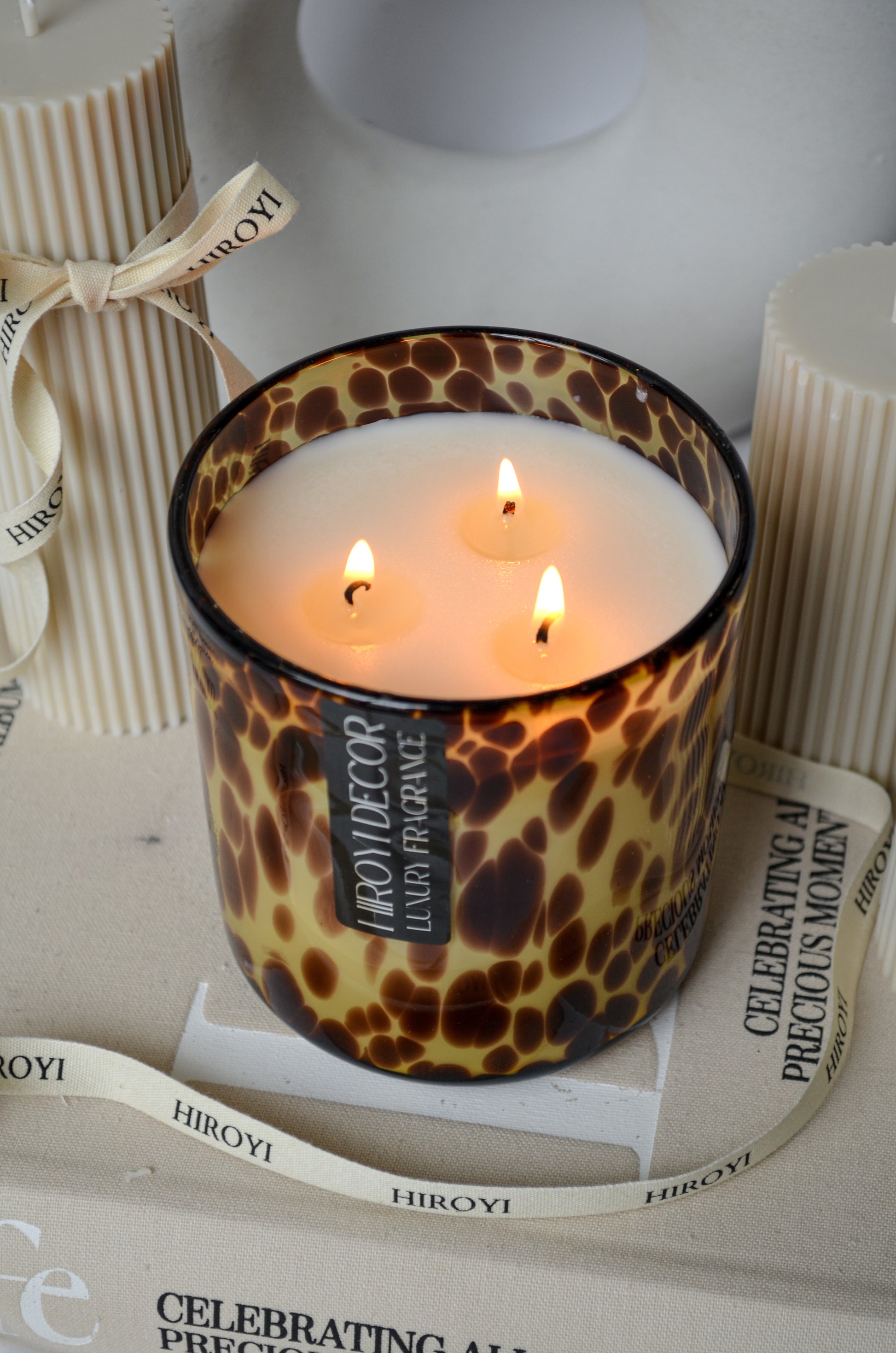 Candle with leopard print design on a surface with 'HIROYI' branding.